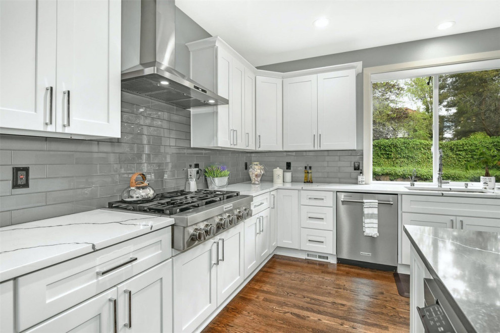 Design ideas for a large transitional u-shaped eat-in kitchen in Seattle with an undermount sink, shaker cabinets, white cabinets, marble benchtops, grey splashback, glass tile splashback, stainless steel appliances, medium hardwood floors, with island, brown floor and white benchtop.