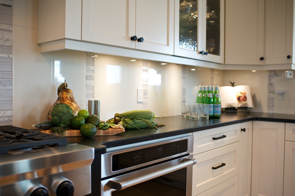 Inspiration for a large transitional u-shaped light wood floor eat-in kitchen remodel in Edmonton with an undermount sink, shaker cabinets, white cabinets, granite countertops, white backsplash, stone tile backsplash, stainless steel appliances and an island