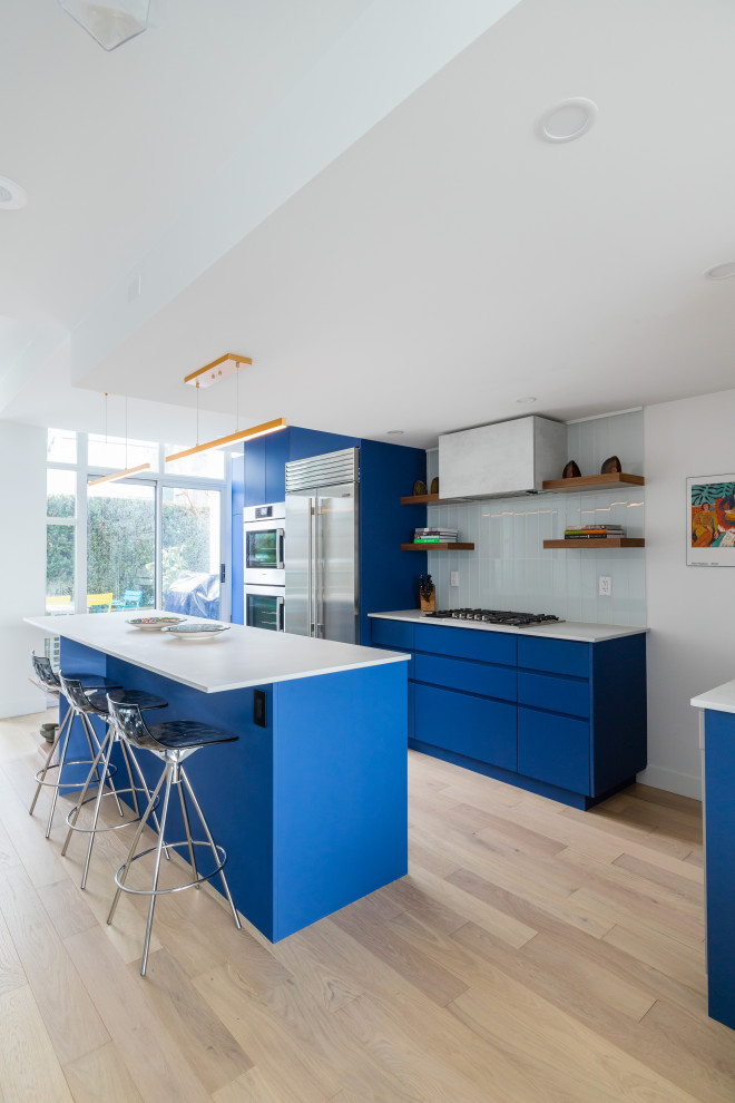 Photo of a large contemporary l-shaped kitchen in Vancouver with flat-panel cabinets, blue cabinets, quartzite benchtops, blue splashback, subway tile splashback, stainless steel appliances, vinyl floors, with island, beige floor and white benchtop.