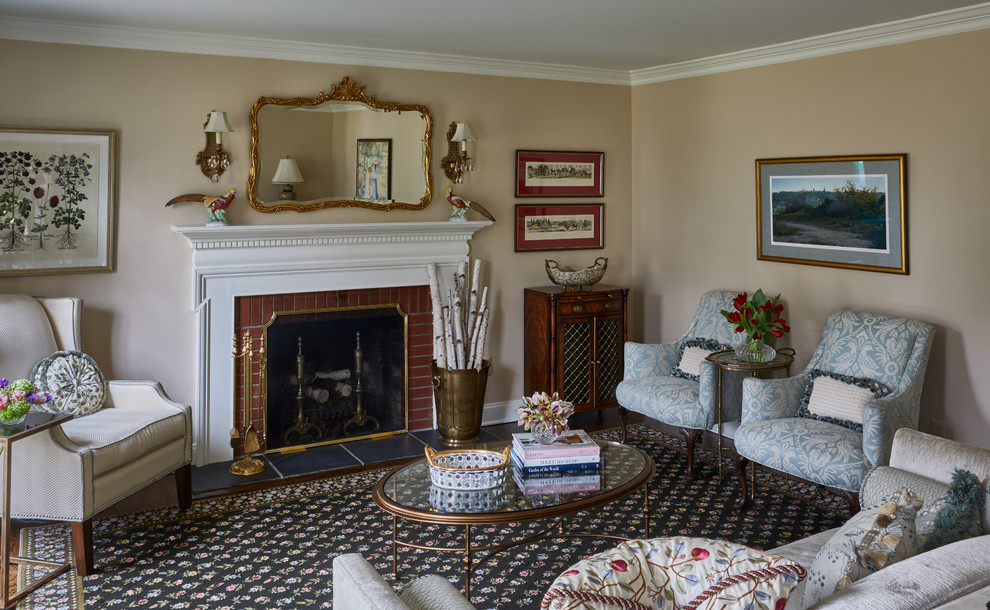 Traditional Rumson Home - Another conversation seating group is arrange around the fireplace with an oversize rug to ground all four upholstered pieces.  The existing red brick fireplace surround was the inspiration to sprinkle pops of red throughout the space; artwork, fabrics, decorative accessories and florals. The larger pieces were kept neutral in color including the area rug, upholstery and wall finish. This helped to temper the space and maintain its formal elegance of a living room.