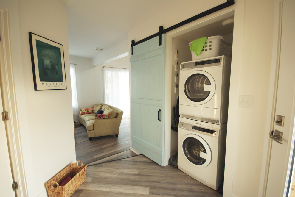 Small beach style laundry cupboard in Miami with white walls, vinyl floors and a stacked washer and dryer.