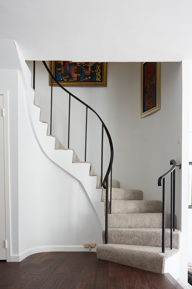 Transitional carpeted curved staircase in New York with carpet risers and metal railing.