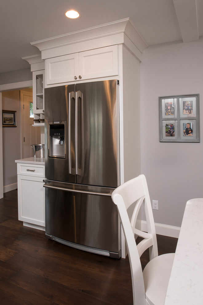 Kitchen - transitional l-shaped dark wood floor and brown floor kitchen idea in Boston with a farmhouse sink, flat-panel cabinets, white cabinets, quartz countertops, white backsplash, ceramic backsplash, stainless steel appliances and an island