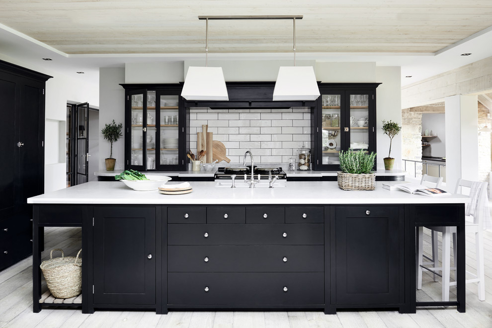 Inspiration for a mid-sized traditional kitchen in London with recessed-panel cabinets, quartzite benchtops, black splashback, subway tile splashback, painted wood floors, with island and white floor.