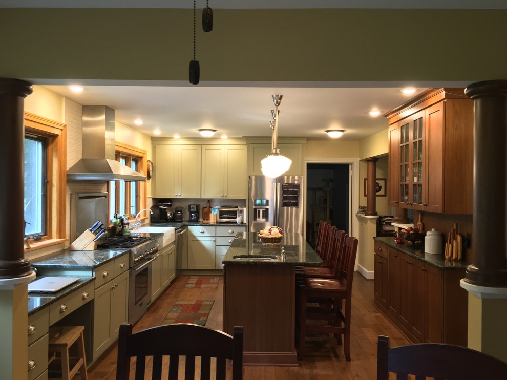 This is an example of a large country u-shaped open plan kitchen in New York with an undermount sink, shaker cabinets, yellow cabinets, granite benchtops, stainless steel appliances, medium hardwood floors, with island, beige splashback and matchstick tile splashback.