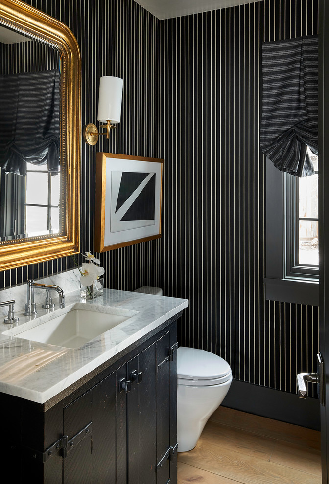 This is an example of a transitional powder room in Other with furniture-like cabinets, black cabinets, multi-coloured walls, light hardwood floors, an undermount sink and white benchtops.