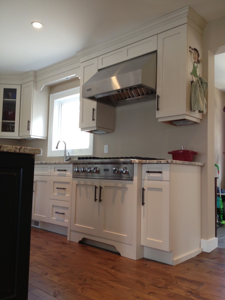 Example of a mid-sized transitional l-shaped medium tone wood floor eat-in kitchen design in Toronto with a double-bowl sink, shaker cabinets, white cabinets, stainless steel appliances and an island