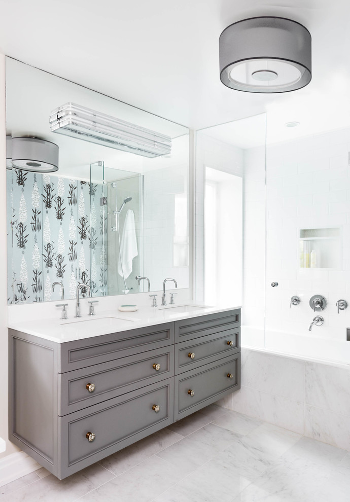 Mid-sized transitional master bathroom in Toronto with an undermount sink, recessed-panel cabinets, grey cabinets, engineered quartz benchtops, an alcove tub, a shower/bathtub combo, white tile, stone tile, white walls, marble floors, white floor, a hinged shower door and white benchtops.