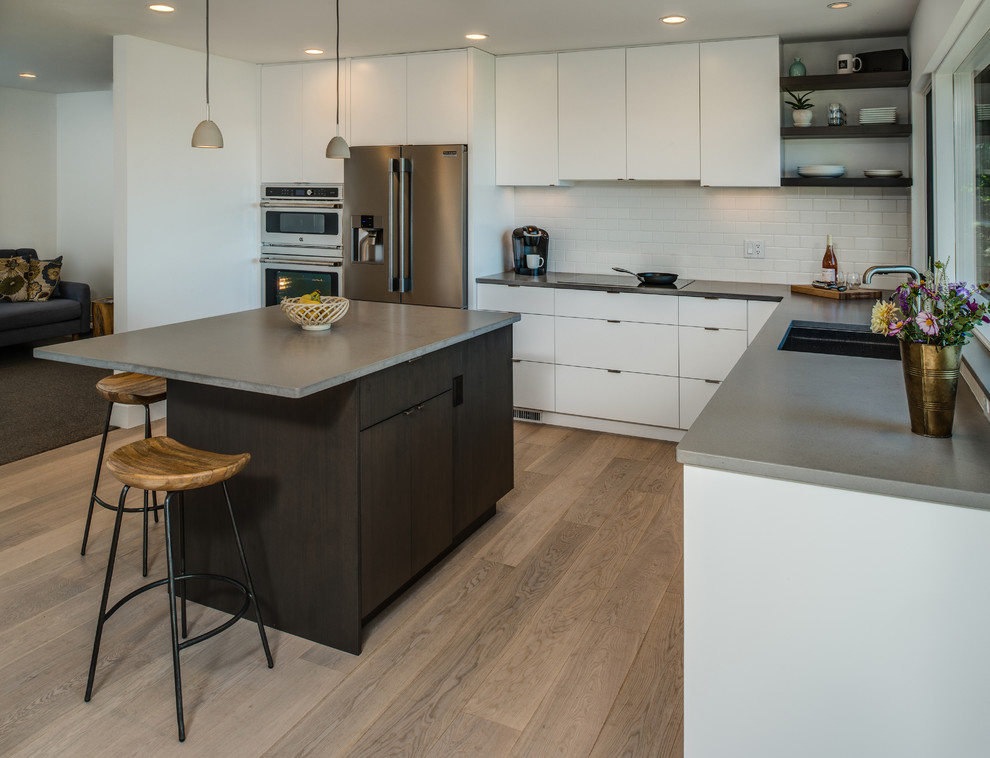 This is an example of a mid-sized contemporary l-shaped separate kitchen in Other with an undermount sink, flat-panel cabinets, white cabinets, concrete benchtops, white splashback, ceramic splashback, stainless steel appliances, light hardwood floors and with island.