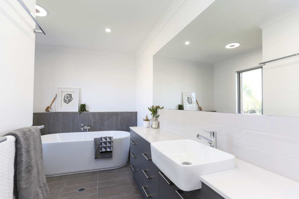 This is an example of a mid-sized scandinavian kids bathroom with flat-panel cabinets, grey cabinets, a freestanding tub, an open shower, gray tile, ceramic tile, white walls, ceramic floors, engineered quartz benchtops, grey floor and an open shower.