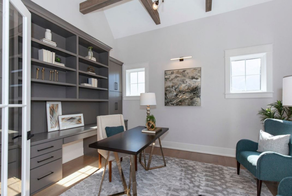 Inspiration for a large country home office in Chicago with a library, white walls, light hardwood floors, a freestanding desk, brown floor and exposed beam.