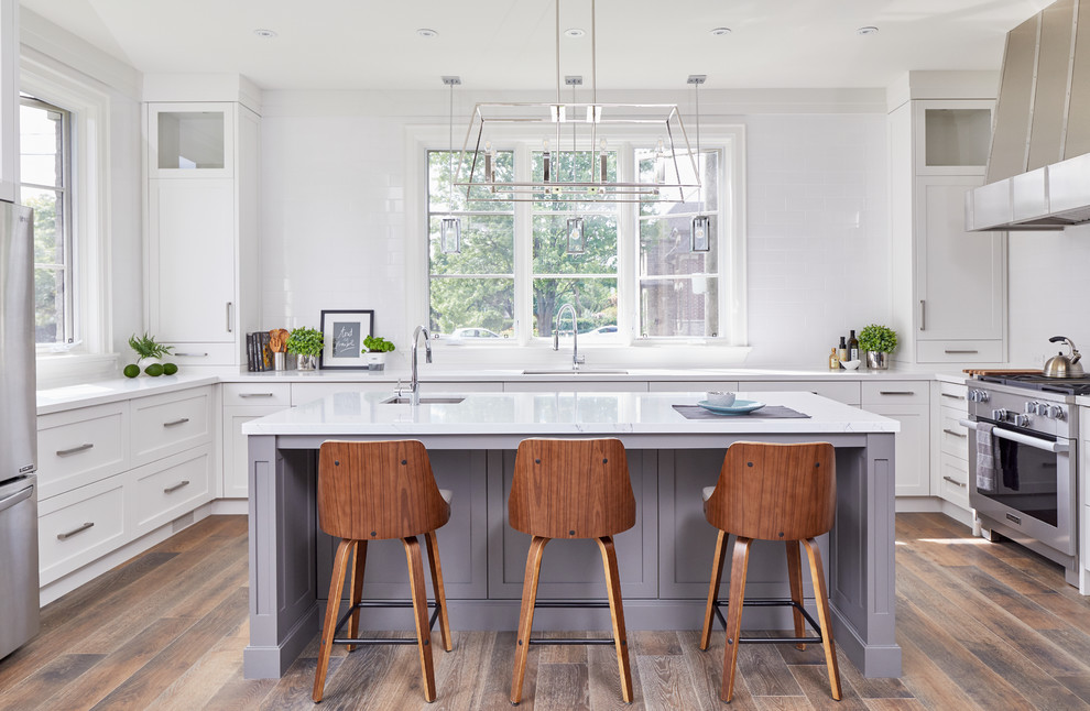 Example of a transitional u-shaped painted wood floor and brown floor kitchen design in Toronto with an undermount sink, shaker cabinets, white cabinets, white backsplash, stainless steel appliances, an island and white countertops