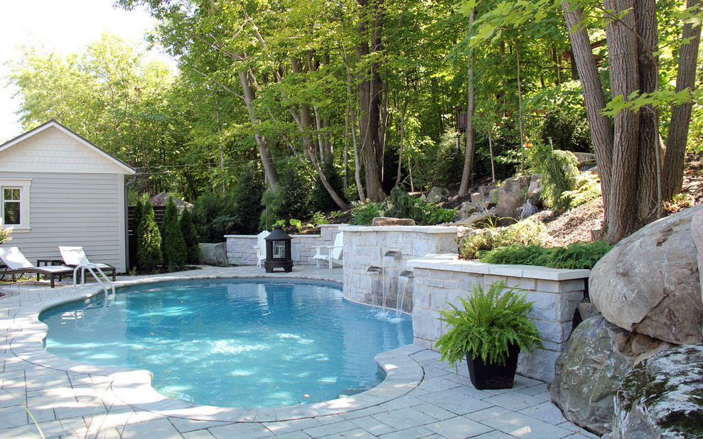 This is an example of a mid-sized traditional backyard custom-shaped pool in Montreal with a water feature and concrete pavers.