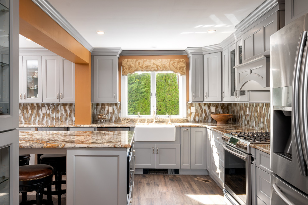 This is an example of a large transitional l-shaped separate kitchen in New York with recessed-panel cabinets, grey cabinets, granite benchtops, with island, yellow benchtop, a farmhouse sink, yellow splashback, glass tile splashback, stainless steel appliances, laminate floors and brown floor.