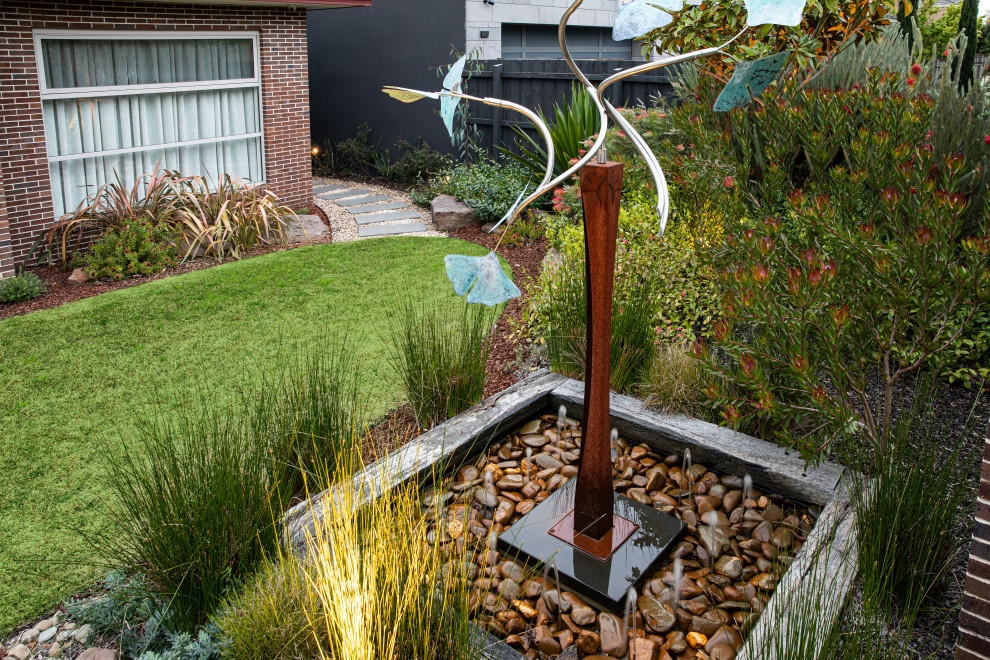 Photo of a mid-sized and australian native contemporary backyard full sun xeriscape for spring in Melbourne with a water feature, natural stone pavers and a wood fence.