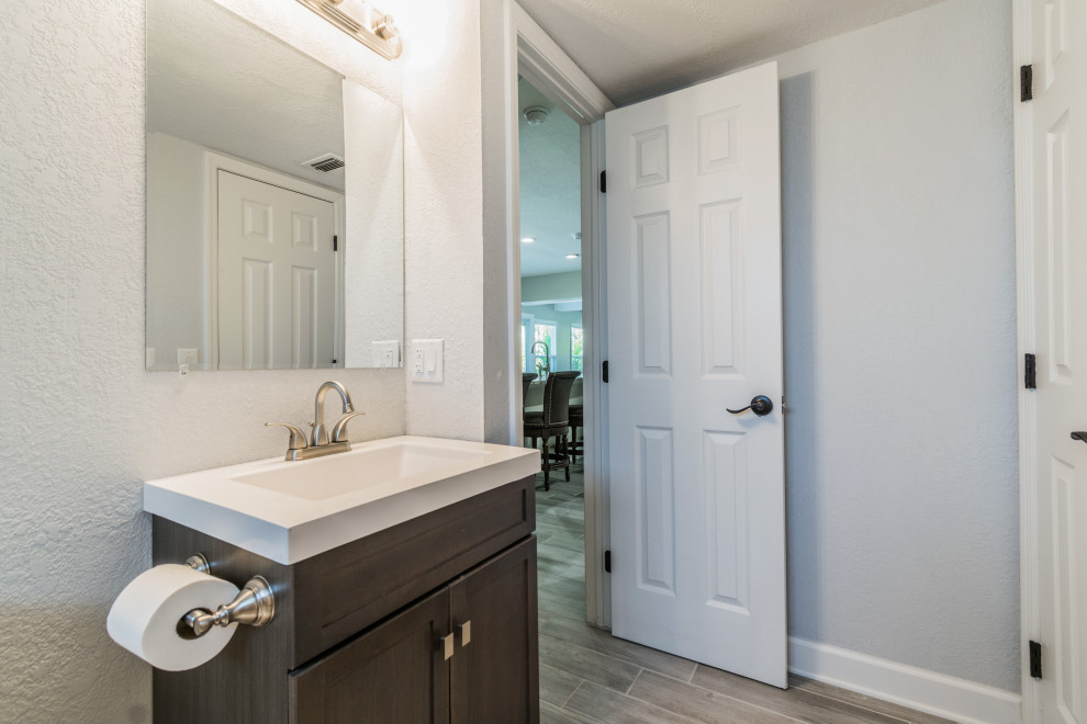 This is an example of a small beach style kids bathroom in Tampa with shaker cabinets, brown cabinets, wood-look tile, engineered quartz benchtops, white benchtops, a single vanity, a freestanding vanity, a drop-in tub, a shower/bathtub combo, gray tile, wood-look tile and grey floor.