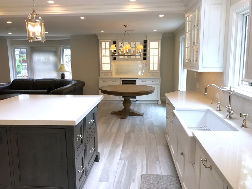 Inspiration for a mid-sized transitional u-shaped light wood floor and brown floor open concept kitchen remodel with a farmhouse sink, recessed-panel cabinets, white cabinets, marble countertops, white backsplash, marble backsplash, stainless steel appliances and an island