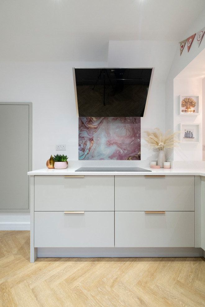 Medium sized contemporary u-shaped kitchen/diner in Cardiff with an integrated sink, flat-panel cabinets, pink cabinets, quartz worktops, pink splashback, glass sheet splashback, stainless steel appliances, laminate floors, a breakfast bar and white worktops.