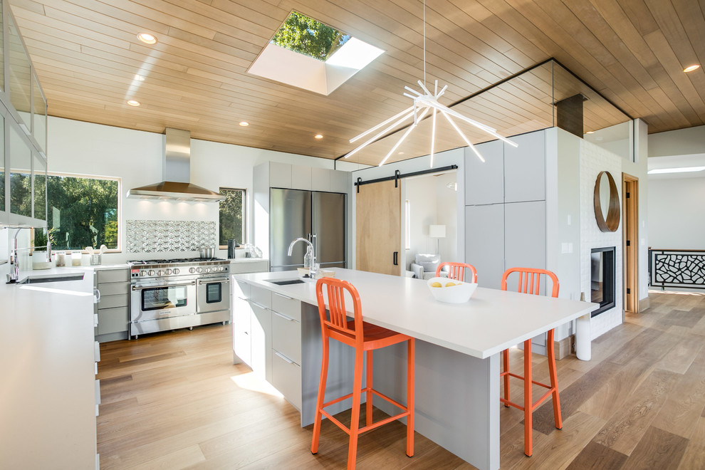 Large contemporary u-shaped open plan kitchen in Seattle with flat-panel cabinets, grey cabinets, metallic splashback, stainless steel appliances, light hardwood floors, with island, brown floor, an undermount sink, quartz benchtops and porcelain splashback.