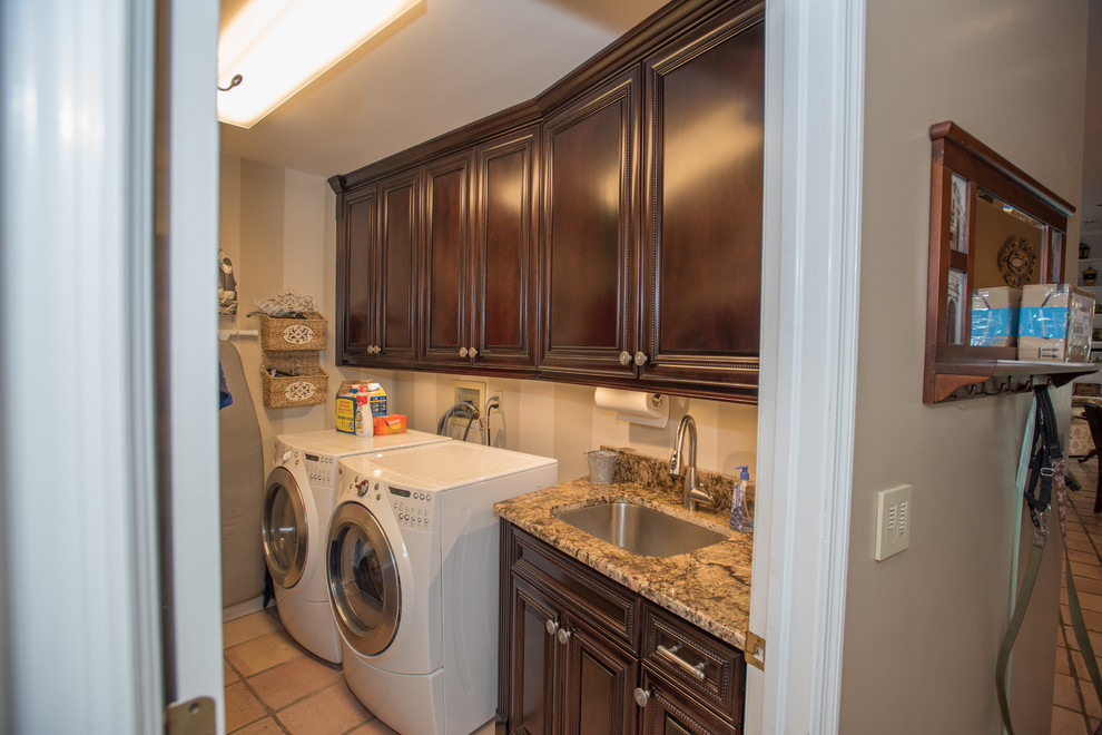 Design ideas for a mid-sized arts and crafts single-wall dedicated laundry room in Tampa with an undermount sink, raised-panel cabinets, dark wood cabinets, granite benchtops, ceramic floors, a side-by-side washer and dryer, beige floor, brown benchtop and brown walls.
