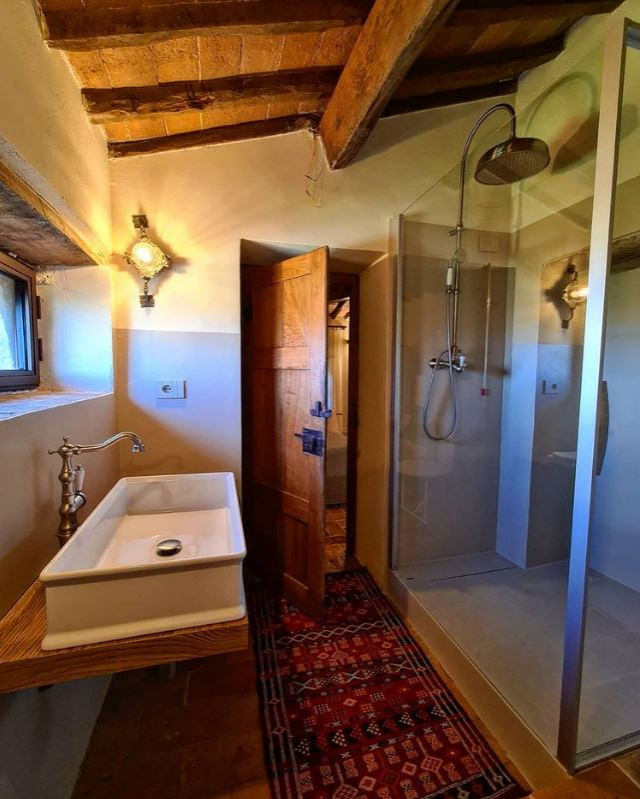 На фото: ванная комната в стиле кантри с угловым душем, унитазом-моноблоком, серыми стенами, полом из терракотовой плитки, настольной раковиной, красным полом, душем с распашными дверями, коричневой столешницей, тумбой под одну раковину, подвесной тумбой и балками на потолке