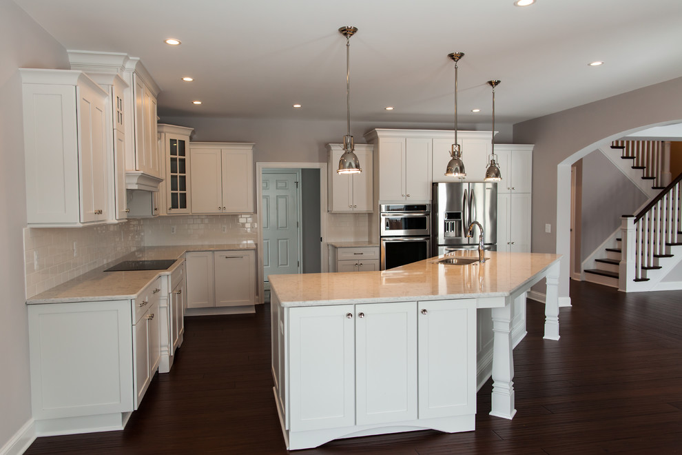 Large transitional l-shaped open plan kitchen in Detroit with an undermount sink, shaker cabinets, white cabinets, quartzite benchtops, white splashback, subway tile splashback, stainless steel appliances, dark hardwood floors, with island and brown floor.