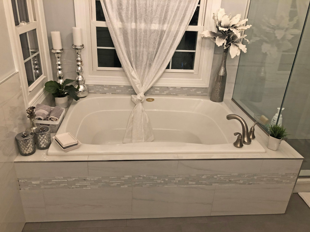 This is an example of a mid-sized transitional master bathroom in Baltimore with shaker cabinets, white cabinets, a drop-in tub, a corner shower, a two-piece toilet, gray tile, marble, grey walls, an undermount sink, engineered quartz benchtops, yellow floor, a sliding shower screen, white benchtops, an enclosed toilet, a double vanity and a built-in vanity.