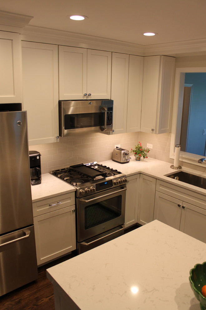Inspiration for a mid-sized transitional l-shaped dark wood floor and brown floor enclosed kitchen remodel in Chicago with an undermount sink, recessed-panel cabinets, white cabinets, quartzite countertops, white backsplash, subway tile backsplash, stainless steel appliances and an island