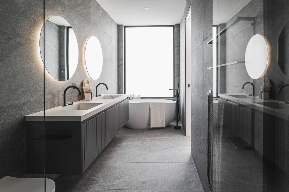 Design ideas for a large modern master bathroom in Melbourne with black cabinets, a freestanding tub, a double shower, a wall-mount toilet, gray tile, porcelain tile, grey walls, pebble tile floors, tile benchtops, grey floor, a sliding shower screen, white benchtops, a double vanity and a floating vanity.