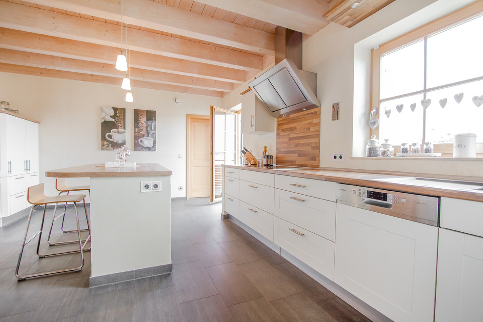 Mid-sized country galley open plan kitchen in Other with beaded inset cabinets, white cabinets, wood benchtops, panelled appliances, ceramic floors, with island, brown floor, brown splashback and timber splashback.