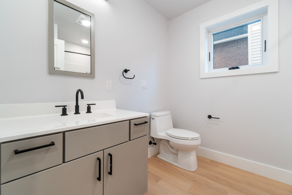 Inspiration för ett mellanstort funkis vit vitt badrum, med släta luckor, grå skåp, ett platsbyggt badkar, en toalettstol med hel cisternkåpa, laminatgolv och beiget golv