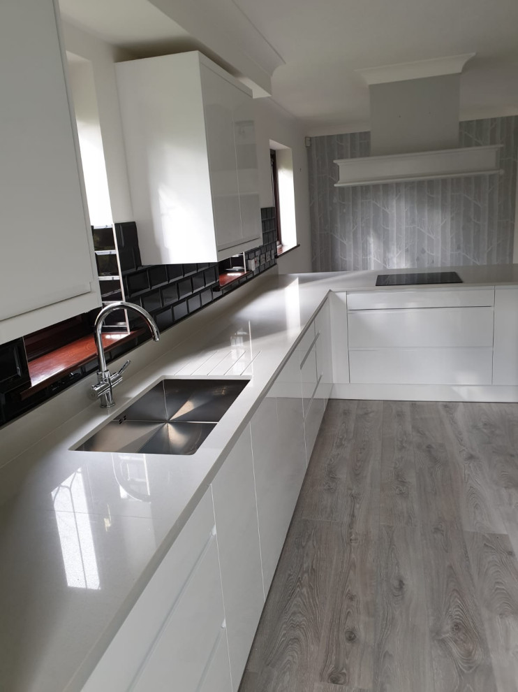 Design ideas for a mid-sized contemporary l-shaped eat-in kitchen in Essex with a single-bowl sink, white cabinets, quartzite benchtops, black splashback, ceramic splashback, black appliances, laminate floors, with island, grey floor and grey benchtop.