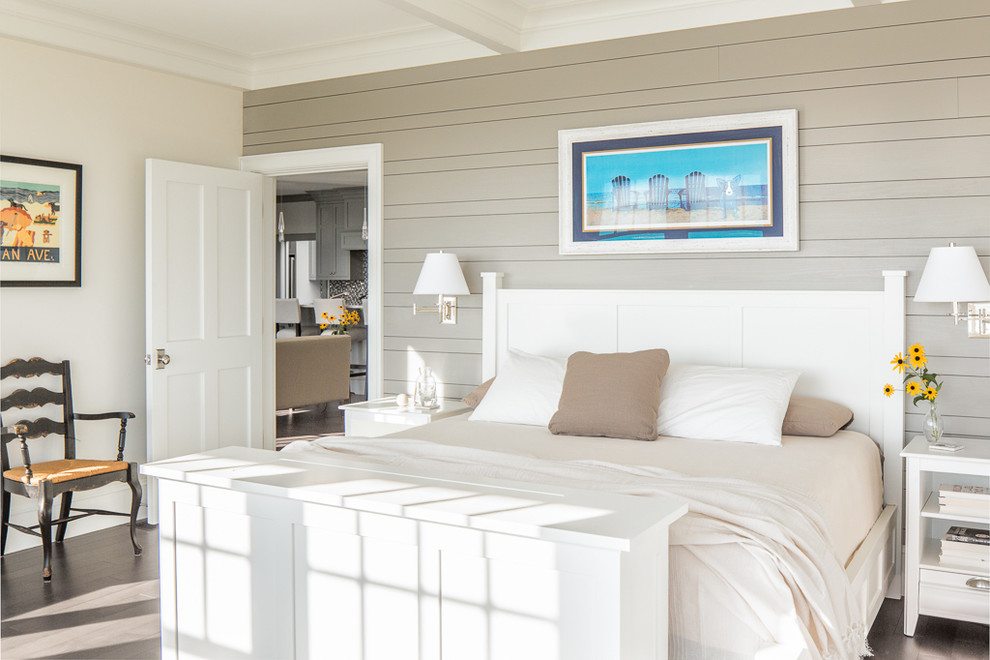 This is an example of a large beach style master bedroom in Portland Maine with beige walls and dark hardwood floors.
