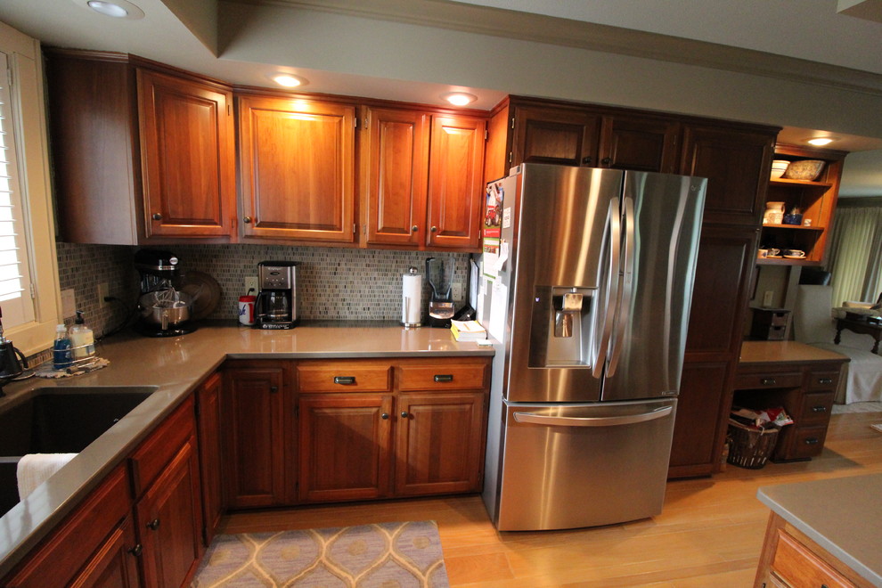 Example of a transitional medium tone wood floor and brown floor kitchen design with an undermount sink, raised-panel cabinets, dark wood cabinets, quartz countertops, multicolored backsplash, stainless steel appliances and brown countertops