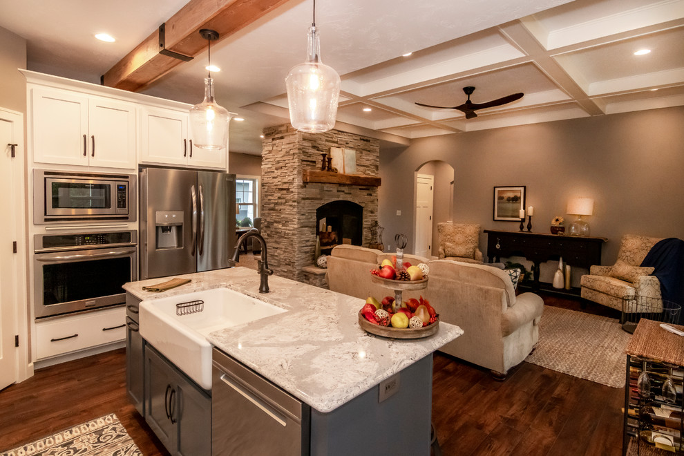 This is an example of a mid-sized arts and crafts l-shaped kitchen pantry in Other with a farmhouse sink, shaker cabinets, white cabinets, granite benchtops, white splashback, porcelain splashback, stainless steel appliances, vinyl floors, with island and beige benchtop.