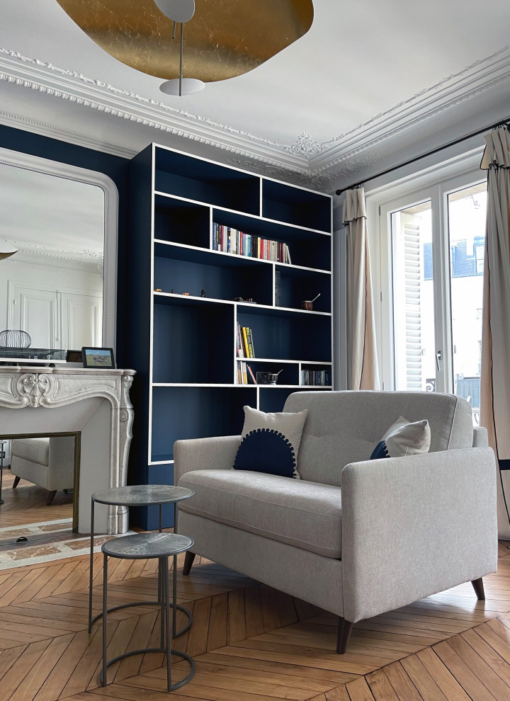 Inspiration pour un salon minimaliste de taille moyenne, ouvert et haussmannien avec une bibliothèque ou un coin lecture, un mur bleu, un sol en bois brun, une cheminée standard et un manteau de cheminée en pierre.