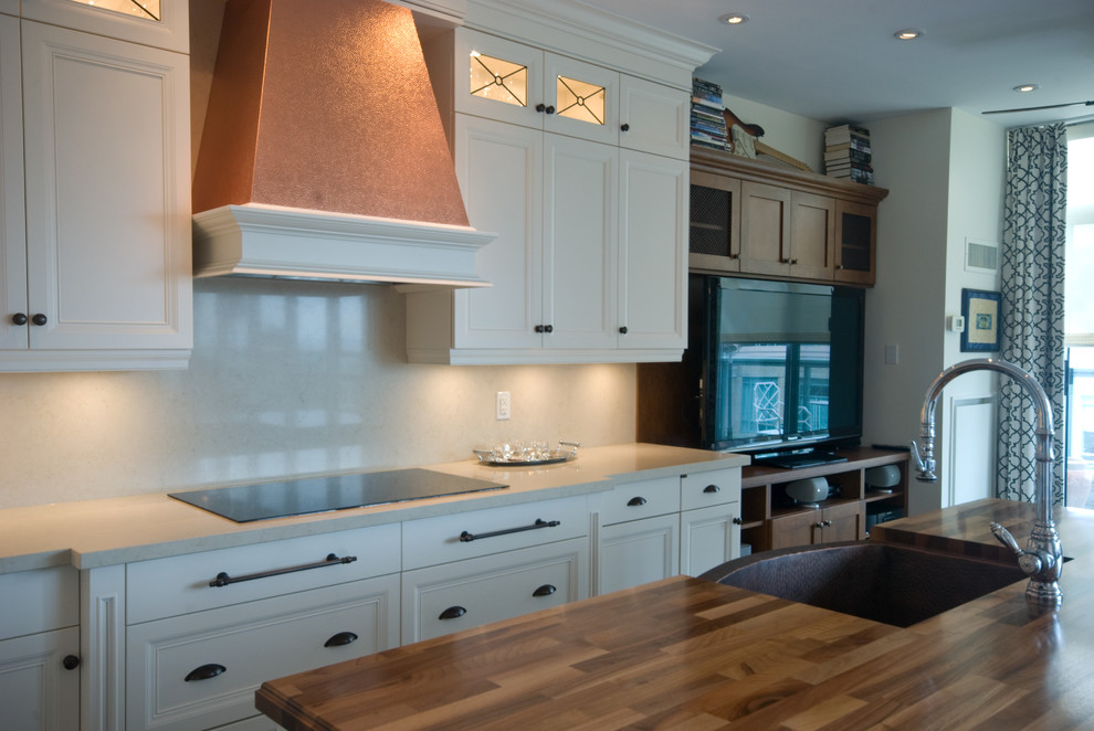 Example of a transitional l-shaped kitchen design in Toronto with a farmhouse sink, recessed-panel cabinets, white cabinets, wood countertops, white backsplash, stone slab backsplash and paneled appliances
