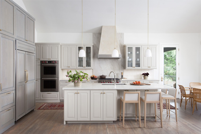 Example of a large transitional l-shaped light wood floor and brown floor open concept kitchen design in Austin with an undermount sink, raised-panel cabinets, gray cabinets, quartzite countertops, beige backsplash, porcelain backsplash, stainless steel appliances, an island and white countertops