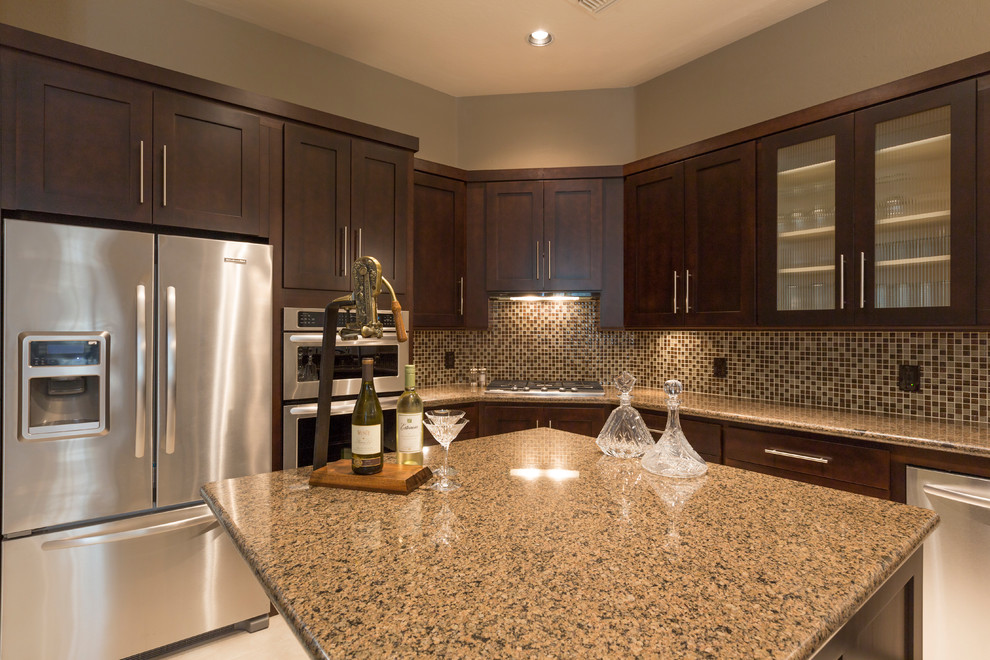 Inspiration for a mid-sized transitional u-shaped travertine floor and beige floor enclosed kitchen remodel in Phoenix with a double-bowl sink, shaker cabinets, brown cabinets, granite countertops, brown backsplash, mosaic tile backsplash, stainless steel appliances and an island