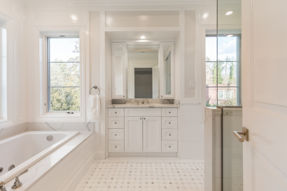 This is an example of a transitional bathroom in New York with shaker cabinets, white cabinets, a drop-in tub, a corner shower, grey walls, mosaic tile floors, an undermount sink, white floor, white benchtops, a single vanity, a built-in vanity and panelled walls.