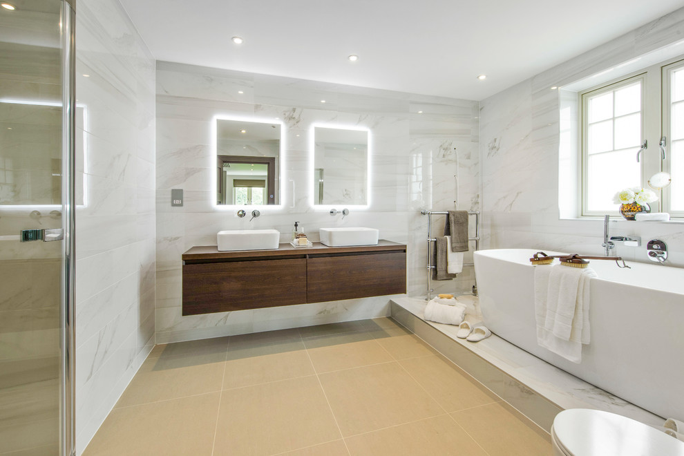Inspiration for a contemporary master bathroom in London with a freestanding tub, a curbless shower, flat-panel cabinets, dark wood cabinets, a one-piece toilet, gray tile, grey walls, a vessel sink, wood benchtops, a hinged shower door and brown benchtops.