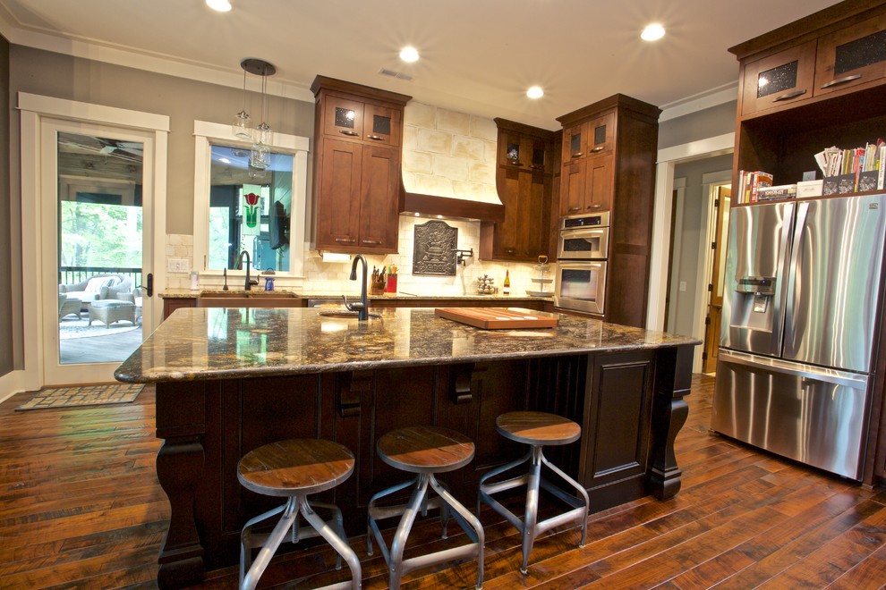 Example of a large transitional l-shaped medium tone wood floor open concept kitchen design with an undermount sink, shaker cabinets, medium tone wood cabinets, granite countertops, beige backsplash, stone tile backsplash, stainless steel appliances and an island
