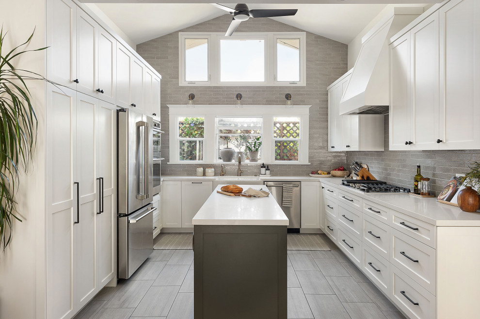 Photo of a mid-sized transitional u-shaped kitchen in San Diego with a farmhouse sink, shaker cabinets, white cabinets, quartz benchtops, grey splashback, ceramic splashback, stainless steel appliances, porcelain floors, with island, grey floor and white benchtop.