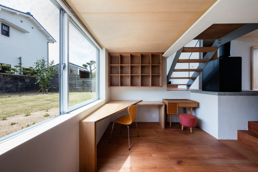 Idéer för att renovera ett mellanstort funkis hemmabibliotek, med vita väggar, plywoodgolv, en öppen vedspis, en spiselkrans i tegelsten, ett inbyggt skrivbord och brunt golv