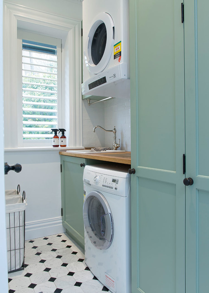 Photo of a large country single-wall utility room in Sydney with recessed-panel cabinets, white walls, a drop-in sink, wood benchtops, marble floors, a stacked washer and dryer, turquoise cabinets and beige benchtop.