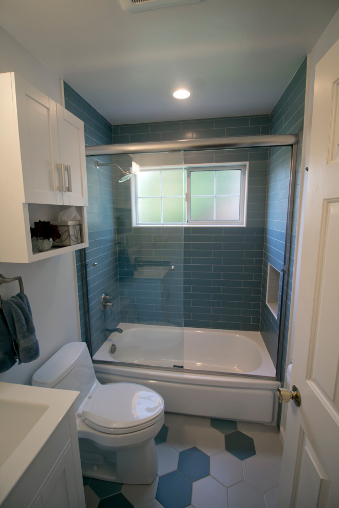 Photo of a mid-sized modern bathroom in San Francisco with shaker cabinets, white cabinets, an alcove tub, a shower/bathtub combo, a one-piece toilet, blue tile, ceramic tile, white walls, ceramic floors, an integrated sink, solid surface benchtops, multi-coloured floor, a sliding shower screen and white benchtops.