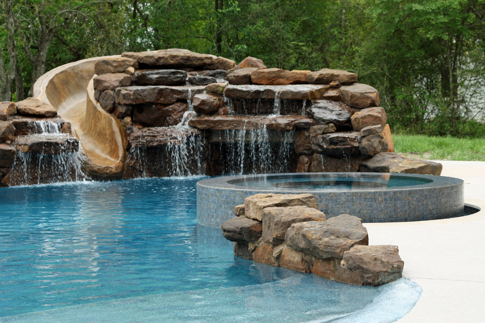 This is an example of a large country backyard custom-shaped pool in Houston with a water slide and natural stone pavers.