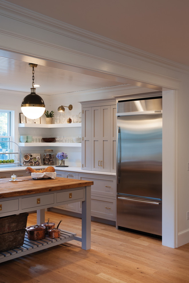 This is an example of a country u-shaped kitchen in Boston with flat-panel cabinets, grey cabinets, white splashback, stainless steel appliances, light hardwood floors and with island.