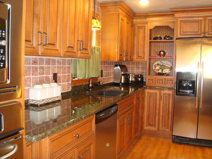 Example of a mid-sized single-wall medium tone wood floor kitchen design in Boston with a double-bowl sink, raised-panel cabinets, medium tone wood cabinets, granite countertops, red backsplash, ceramic backsplash and stainless steel appliances
