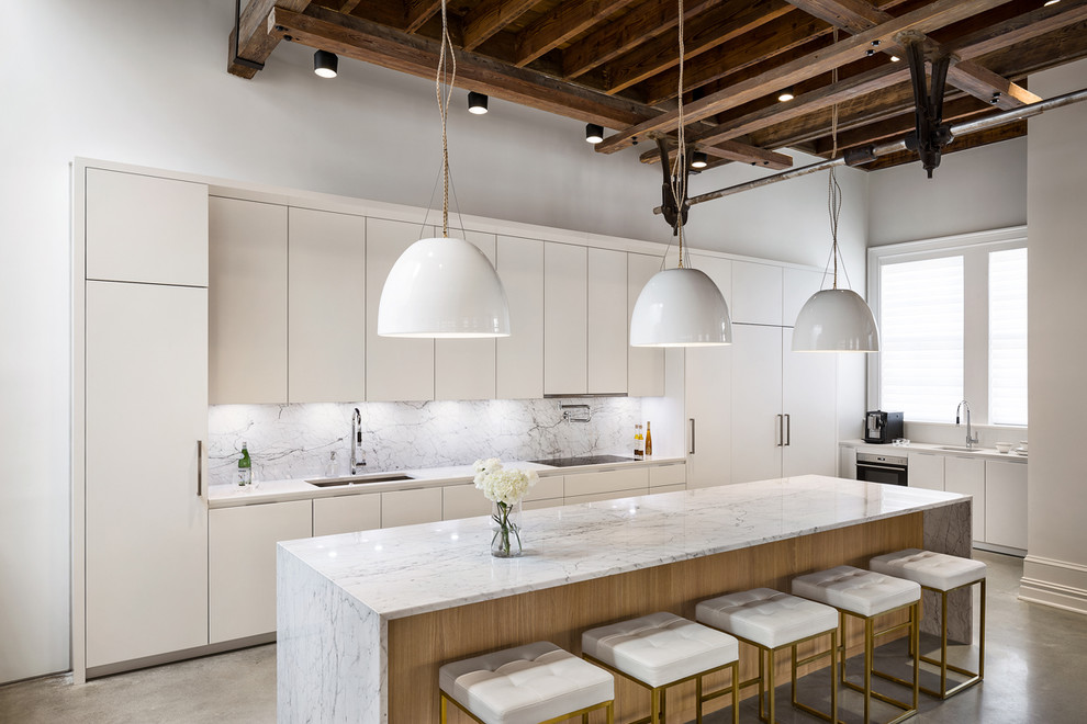 This is an example of a large contemporary galley kitchen in New York with an undermount sink, flat-panel cabinets, white cabinets, marble benchtops, white splashback, marble splashback, panelled appliances, concrete floors, with island, grey floor and white benchtop.